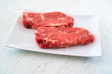 Marble beef striploin steak on a white plate on a marble countertop.