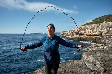 Latin woman, middle-aged, wearing sportswear, training, doing physical exercises, plank, sit-ups, climber's step, burning calories, keeping fit, outdoors by the sea, wearing headphones, smart watch