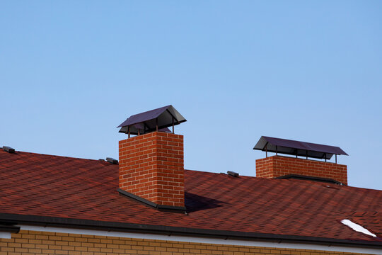 The Roof Of The Cottage To The Slopes, The Flashings, Chimney On Background Of Blue Sky. Brown Roof Of Bituminous Tiles. Flexible Single