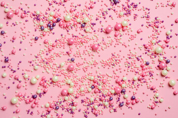 Many small multi-colored sweet balls on a pink background. Pink abstract background. Focusing in the center of the frame.