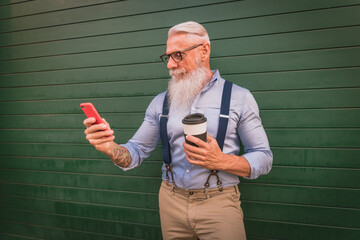 an older man in hipster clothes and glasses and a long white beard with a coffee cup and a phone,...