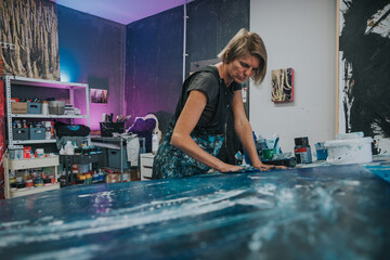 Young woman paints an abstract picture with her hands and spatula on a work table in her interior studio. Focus on head