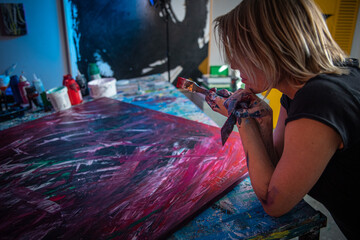 Young woman paints an abstract picture with her hands in her interior studio, focus on hands
