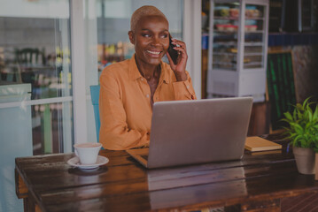 black adult woman talks on her phone while working on her computer in a coffee shop focus on the face