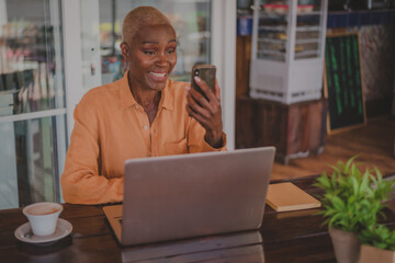 black adult woman talks on her phone while working on her computer in a coffee shop focus on the face