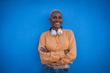 an adult black woman poses with headphones on a blue wall and smiles