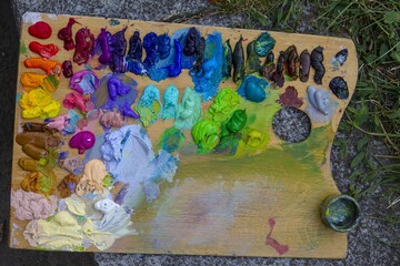 artist wooden palette, mess of fresh squeezed bright colorful oil paints mixed in disorder, outdoor painting plein air, creativity vibrant inspiration postcard