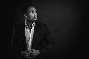 Fototapeta na wymiar Portrait of an attractive, handsome, stylish professional African American businessman in a stylish suit and white shirt, isolated on a dark background, looking away. Low key. Selective focus