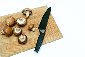 Close up of fresh mushrooms and knife on wooden cutting board in kitchen