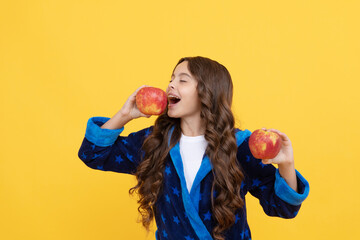 happy kid girl in sleepwear biting fresh apple fruit, organic food