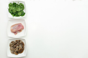Isolated on a white background there are 3 white plates with different types of animal and vegetable. Plates include fresh green spinach leaves, chicken and pickled mushrooms. Have place for text