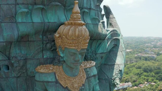 Face of Hindu deity Vishnu in Garuda Wisnu Kencana statue in Bali, Indonesia. Close up aerial view of religious figure on large copper statue rising above the city