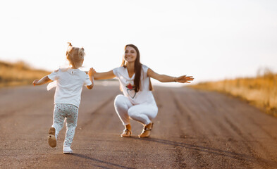 A little girl in a white T-shirt runs to meet her mother. Back view.