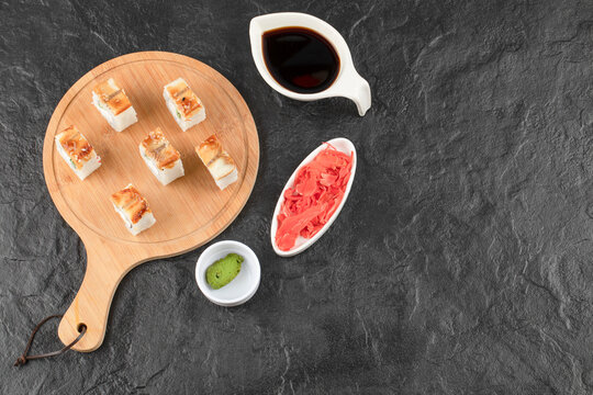 Sushi rolls with eel on wooden board with soy sauce and ginger