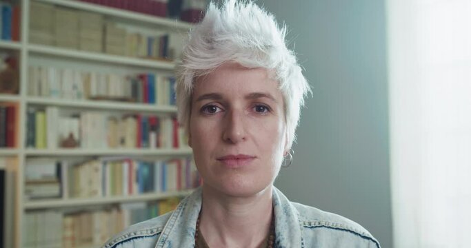 Cinematic shot of an young attractive happy transgender man with alternative haircut style is smiling in camera in a living room at home. Concept of gender expression, identity and diversity.