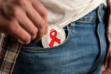 Close up of young man taking condom out of pocket in jeans. Remember about protection. Safe sex, AIDS. Pulling out condom gold color. Safety sex concept. Contraception. Contraceptive. World AIDS day