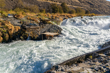 Shearers Bridge, Oregon - 11/2/2020:  A native American Indian man fishing for salmon in the Deschutes River Rapids at Shearers Bridge with a dip net from a wooden platform, near Tygh Valley Oregon