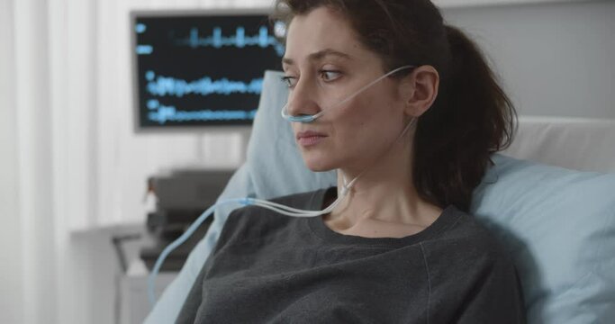Portrait upset young woman patient with nasal cannula delivering oxygen resting in bed at hospital
