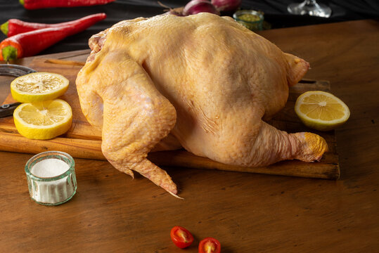 Whole raw chicken from the field, yellow and natural on wooden table with lemon, tomato and onion and seasonings.