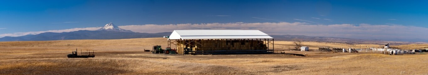 Fototapeta na wymiar A panorama image of a hay storage barn and farm equipment and rodeo grounds and on a farm near Dufur Oregon with Mt Hood in the background.