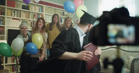 Cinematic shot of happy smiling family members with colorful balloons making family photo portrait together with camera on tripod with timer during celebration son brother graduation party at home.