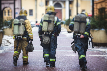 Group of fire men in uniform during fire fighting operation in the city streets, firefighters with the fire engine truck fighting vehicle in the background, emergency and rescue