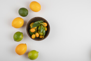Bowl of fresh kumquats, limes and lemons on white background