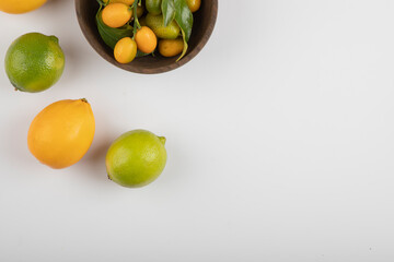 Bowl of fresh kumquats, limes and lemons on white background
