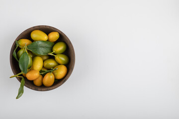Wooden bowl of yellow kumquats with leaves on white background