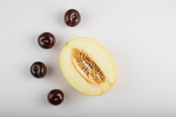 Delicious ripe plums with halved melon on white background