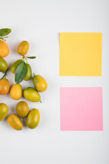 Yellow kumquats with leaves and memo pads on white background