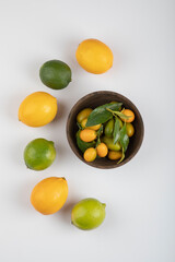 Bowl of fresh kumquats, limes and lemons on white background