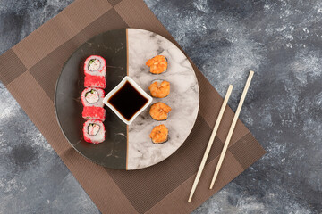 Two kinds of tasty sushi rolls and soy sauce on marble plate