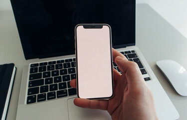 Man holding 2020 smartphone over 2020 laptop on modern business desk - Phone Mock Up- Perspective