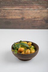 Wooden bowl of yellow kumquats with leaves on white background