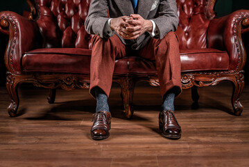 Business partner in a classic suit, sitting on a red vintage sofa. .Hands clenched, close-up.
