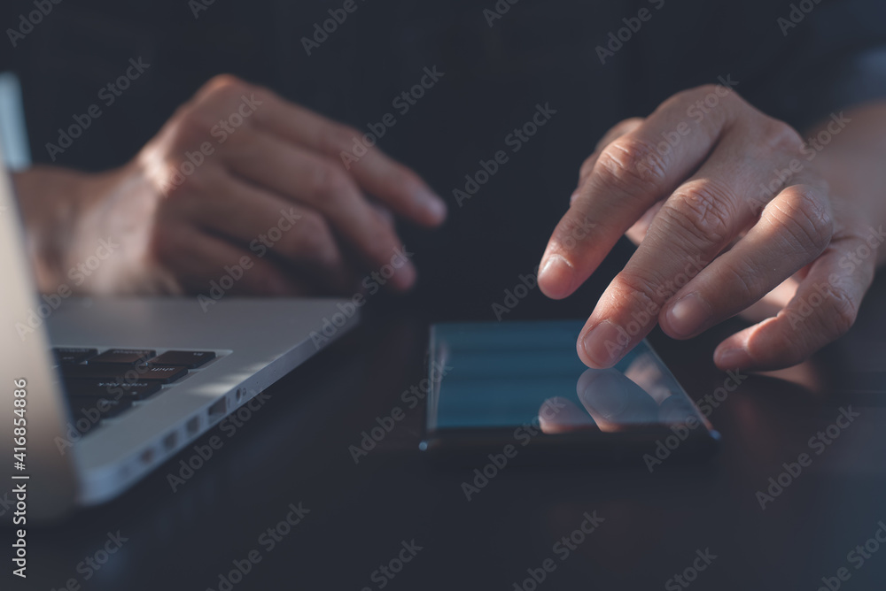 Poster closeup of man finger touching on mobile smartphone screen and working on laptop computer on office 