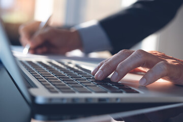 Close up of man hand working on laptop computer, searching information and writing on notepad in...