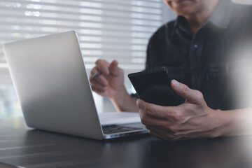 Man using mobile smartphone during working on laptop computer from home office, close up