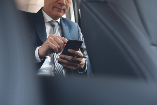 Middle Age Asian Businessman Using Mobile Phone Inside A Car During Going To Workplace In The Morning