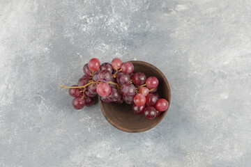 Wooden bowl of fresh red grapes on marble surface