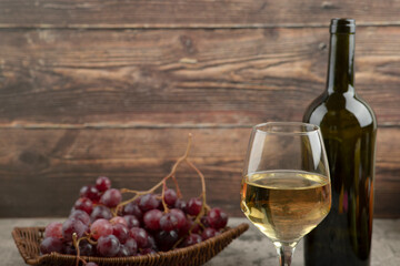 Wicker basket of red grapes with glass of white wine on marble table