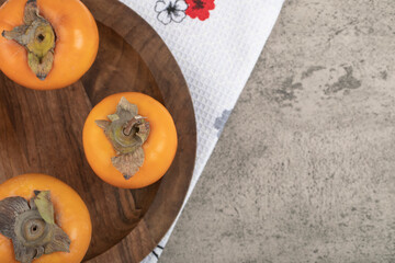 Delicious ripe persimmon fruits placed on wooden plate
