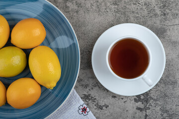 Cup of hot tea and plate of fresh lemons on stone surface