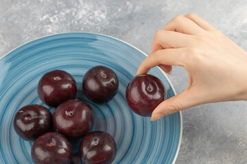 Female hand taking fresh plum from blue plate