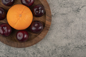 A wooden plate of fresh purple plums with healthy orange