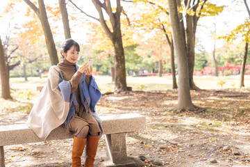 秋の公園でスマホを持った女性
