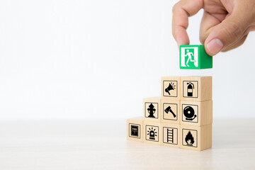 Close-up hand choose wooden toy blocks stacked with door exit sing icon with fire extinguisher and fire protection symbol for safety prevent and protect accident of emergency and rescue.