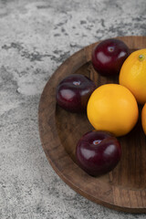 A wooden plate of purple plums and fresh lemons on stone background