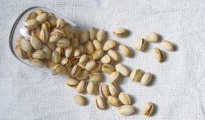 Organic pistachios in glass scattered on burlap background, healthy snack, top view